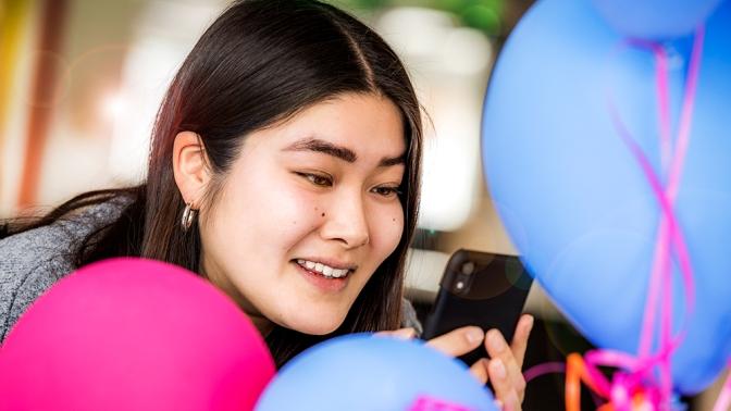 En tjej sitter med sin mobil bland ballongen