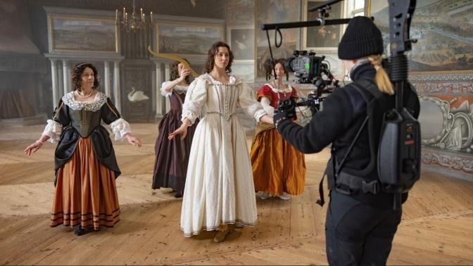 En kameraperson spelar in en scen med fyra dansade personer i klänningar.