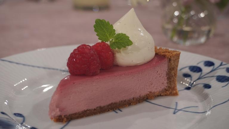 En rosa cheesecake med smak av hallon ovanpå en blåvit tallrik.