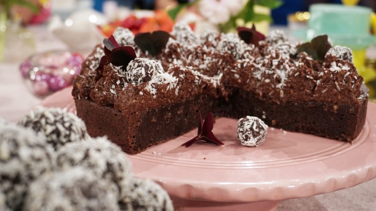 Kladdkaka med chokladbollsglasyr på ett rosa tårtfat med chokladbollar på och bredvid bild.