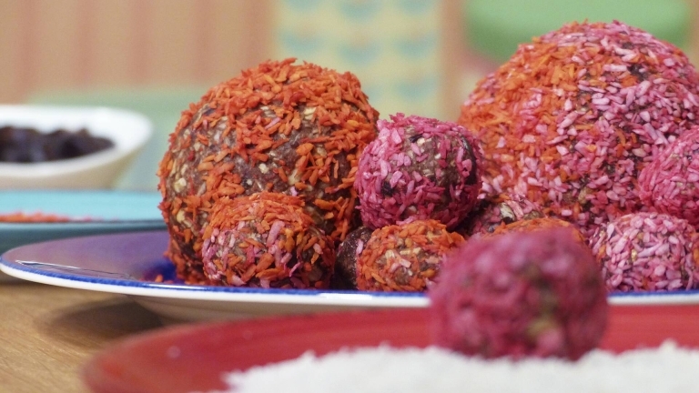 Chokladbollar och rawfoodbollar rullade i orange och rosa kokos på en tallrik.