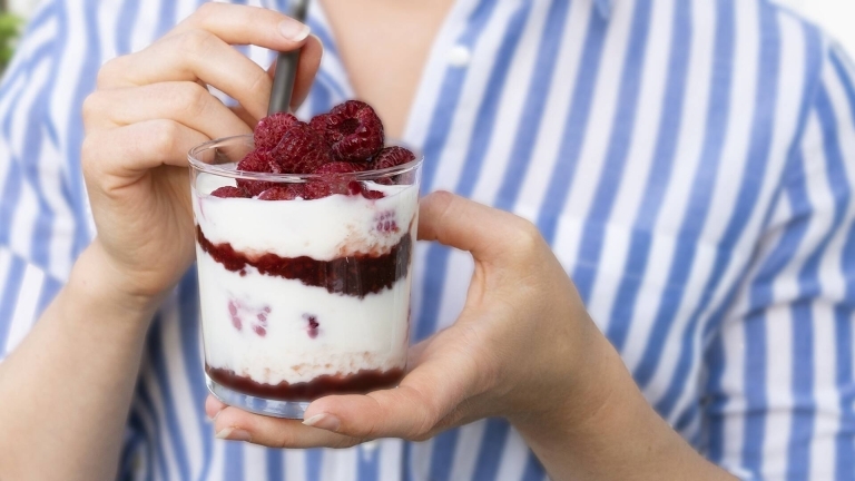 Hallon i en skål med yoghurt hålls upp av en perosn i blåvitrandig skjorta. 