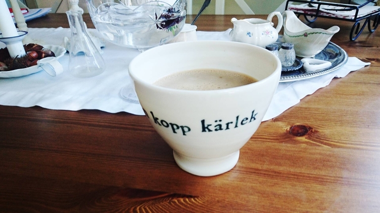 En kaffekopp med kaffedryck i en vit kopp på ett träbord.