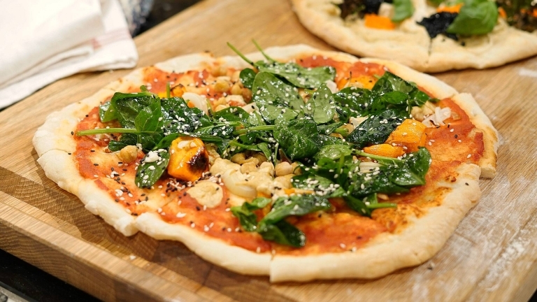 En träbricka med en pizza med kikärter, pumpa, spenat och sesamfrön.