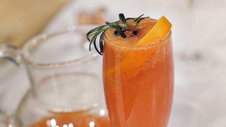 Ett champagneglas med alkoholfritt mimosa, garnerad med en skiva blodapelsin och färsk rosmarin.