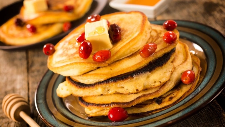 Amerikanska pannkakor staplade på varandra på ett fat. På toppen en klick smör och röda bär. 