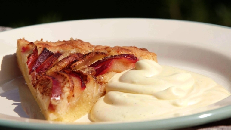 En pajbit med äppel och plomma på och vaniljkräm i en tallrik.