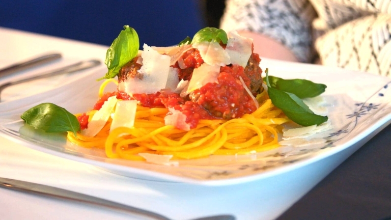 Pumpaspagetti med köttbular, tomatsås, några blad basilika och några skivor parmesan ost.