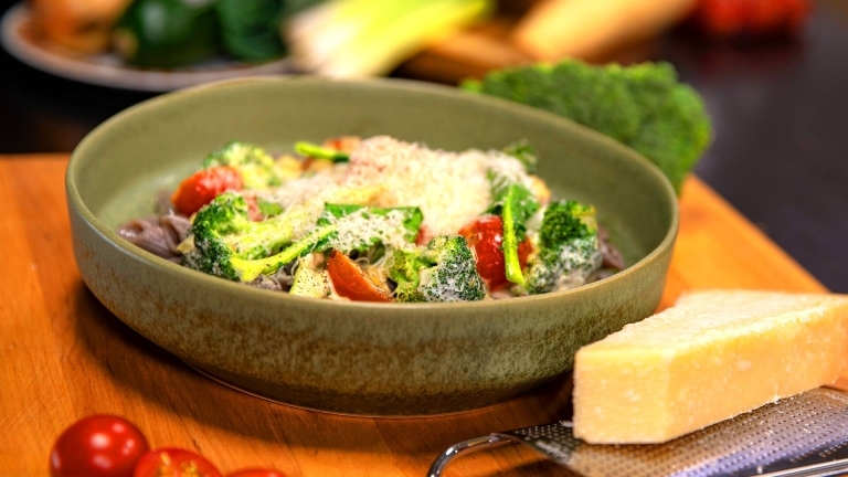 Bönpasta med broccoli , parmesan ost och grönsaker  på en skål och hel parmesan ost i bredvid.