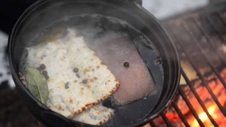 En kittel på ett grillgaller värmer en fläskbit och ett tunnbröd. 