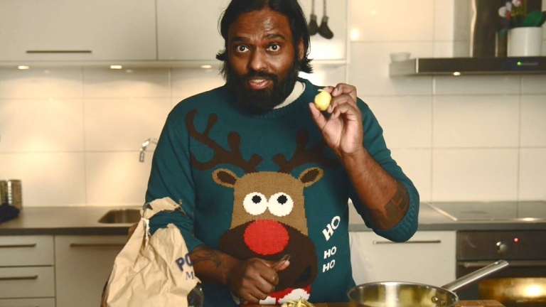 En man håller upp en potatis. Han har en jultröja med en ren på sig. 