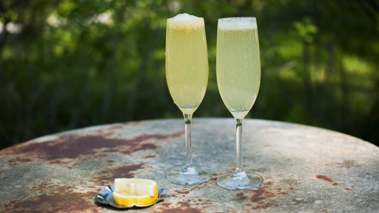 två fyllda champagneglas på plåtbord utomhus, citronskivor.