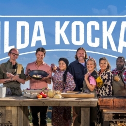 en klarblå himmel syns med texten "Vilda kockar" i bakgrunden, i förgrunden står deltagarna bakom ett stort träbord med diverse mat och skärbrädor.