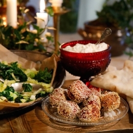 Bollar med rödbetsfalafel på glasfat. Bredvid står röd skål med äppelyoughurt och ett fat med stekt kål, samt libanesiskt bröd. 